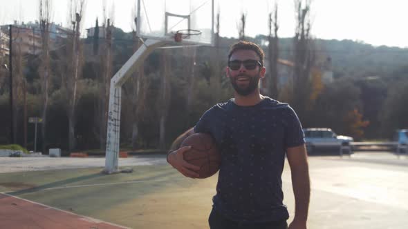 Male basketball player stands with ball under arm after training handheld video portrait