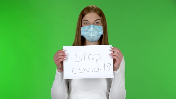 Portrait of Young Girl in Medical Protective Face Mask Looking at Camera and Holding a Poster Stop