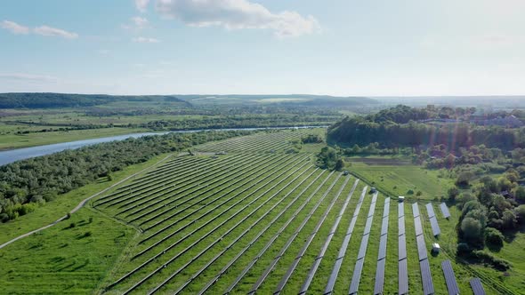 Aerial view on Solar Power Station in Green Field near River at Sunny Day