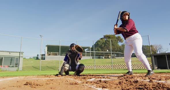 Diverse group of female baseball players playing on the field, hitter swinging for pitched ball