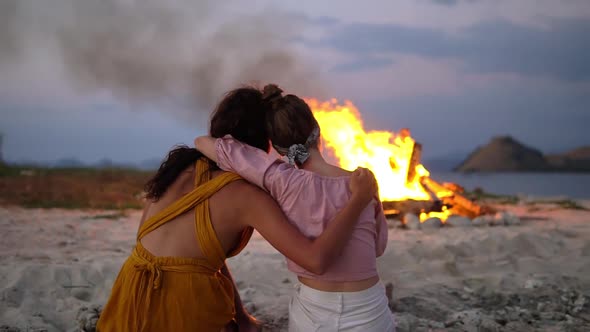 Two Female Lovers Sitting Embracing on the Beach Near a Burning Fire Romantic Couple Enjoying Each