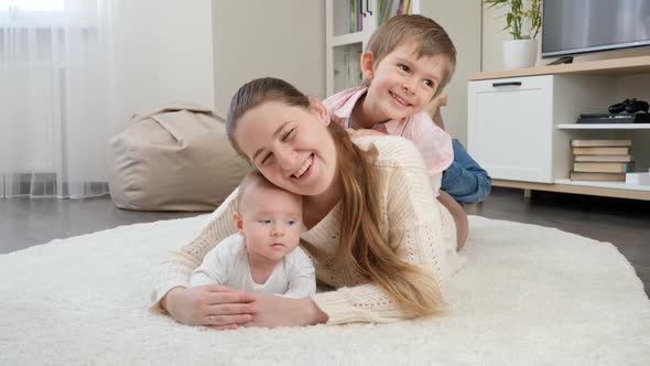 Happy Smiling Children Hugging and Having Fun with Mother on Carpet in Living Room