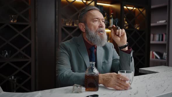 Thoughtful Mature Businessman Enjoying Cigar Relaxing with Glass of Whiskey at Bar Counter Slow