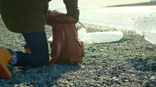 Man In Green Winter Jacket Looking Through Brown Leather Backpack Pulls Out Camera  Takes Picture