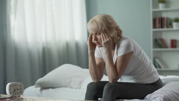 Senior Woman Sitting on Bed and Suffering From Terrible Headache, Health Problem