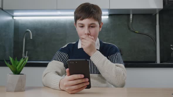Afraid and Shocked Boy Look at Smartphone Screen Cover Mouth with Hand at Home Kitchen