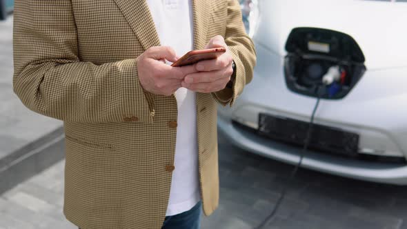 Senior Businessman Using Smart Phone and Waiting Power Supply Connect to Electric Vehicles for