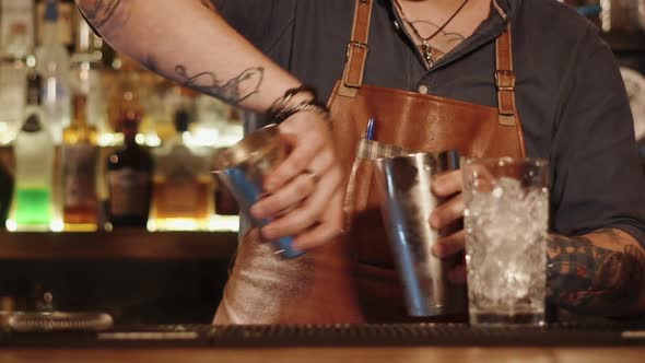 Man Standing Behind a Bar Rack Is Transfusing Cocktail From One Cup To Other