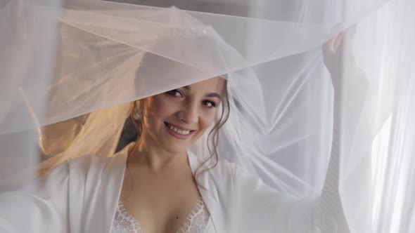 Bride in Boudoir Dress Under Veil and in a Silk Robe. Wedding Morning Preparations Before Ceremony