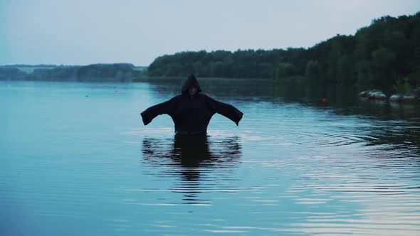 Evil witch in black cloak with hood in the river. Halloween costume.