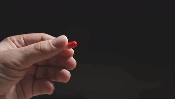 Close-up of a Man's Hand, Two Fingers Holding a Capsule on a Dark Background