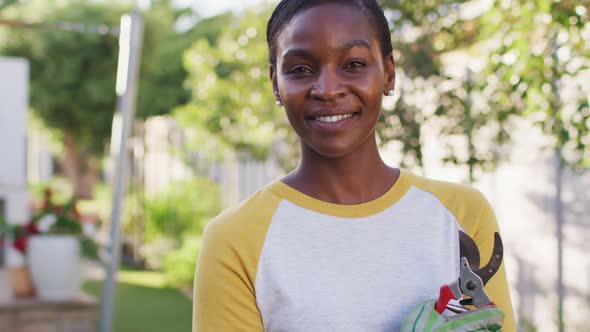 Portrait of african amercian woman holding secateur looking to camera and smiling in garden