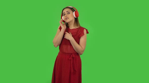 Tender Girl in Red Dress Is Dancing and Enjoying Music in Big Red Headphones. Green Screen