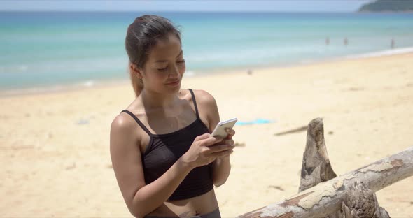 Ethnic Sportswoman Using Smartphone on Beach