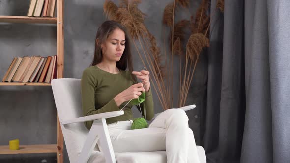 Focused Latin Woman Holding Needles Sitting on Armchair and Enjoying Knitting