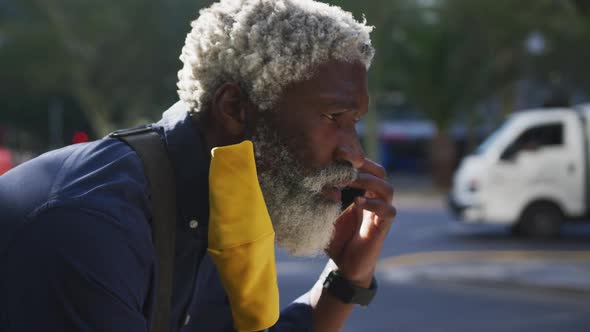 Close up of african american senior man wearing face mask talking on smartphone on the road