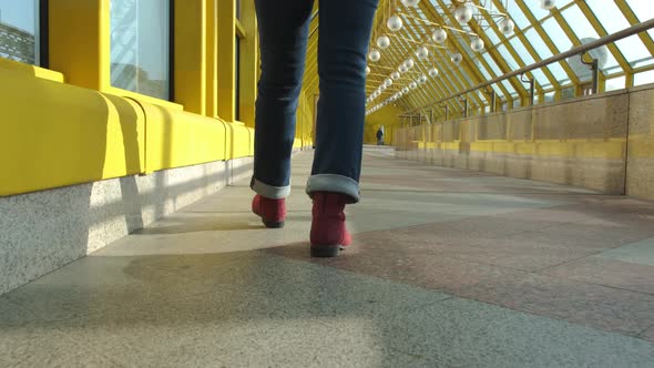 Women's Legs in Burgundy Boots and Blue Jeans Walk on a Closed Pedestrian Bridge