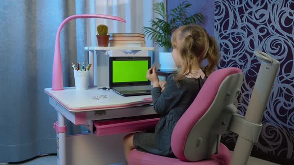 Child Schoolgirl Learns Lessons Being at Home Using Digital Laptop Computer with Green Screen