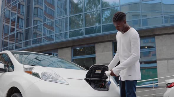 A Young African American Man Connects an Electric Car to the Charger