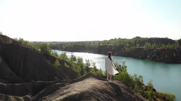 Nice Slender Woman in Long White Dress Approaches Edge of Abyss and Spreads Her Arms to Sides She