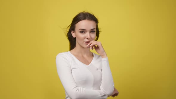 Sexy Woman in White Tshirt on Yellow Background Playfully Looks at Camera Her Hair Flutters in Wind