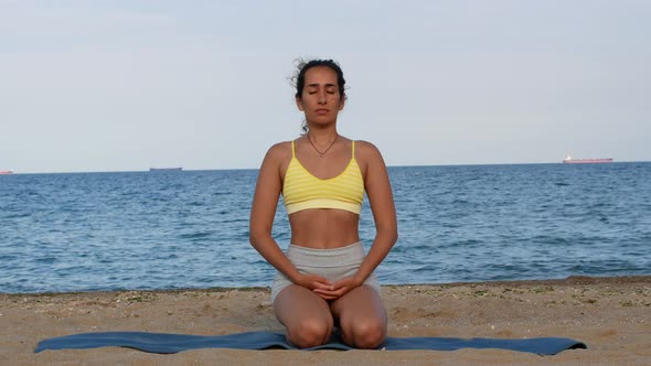 Beautiful tanned young woman sitting in a meditation pose on the beach. Goods for health.