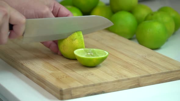 Hand Slicing fresh Lime With Knife On Wooden Board In Kitchen