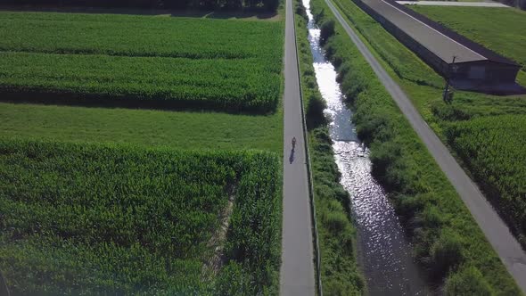 Aerial view of a young man riding a bicycle in Sugana Valley, Italy with camera tilting down as bike