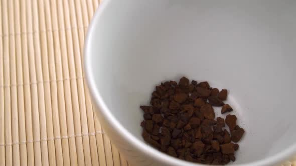 Instant chicory falls into a white steaming cup in slow motion