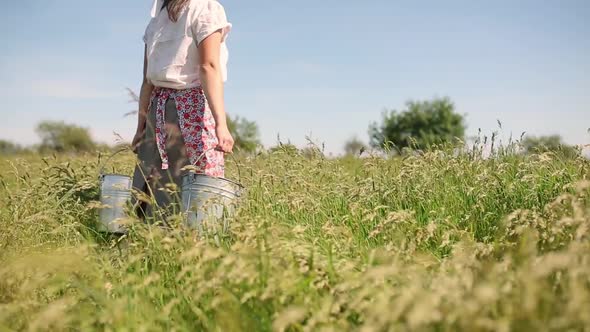 Closeup of a Milkmaid Carrying Buckets and Walking Through Tall Grass