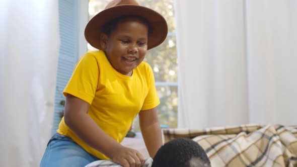 Excited Little African Boy Playing with Father at Home Riding His Back