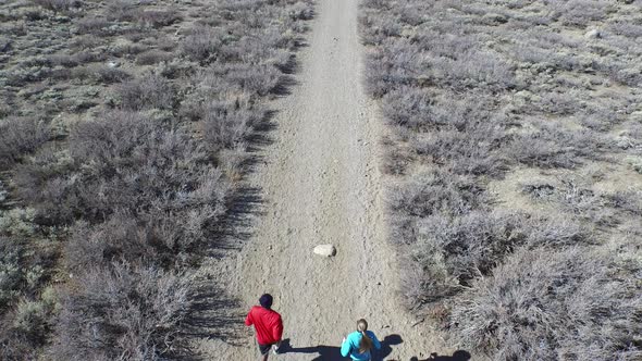 Aerial shot of a young man and woman trail running with dog on scenic mountain trail