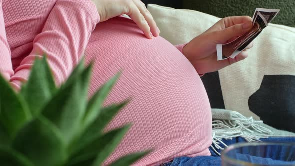 A beautiful pregnant woman holds and watches an ultrasound photo of her newborn baby.