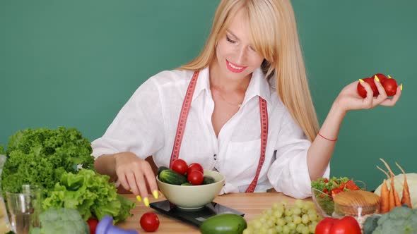 Fit Woman Measuring Vegetabes on Scales at a Table on Green Background