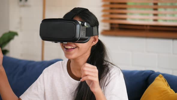 Portrait of a young Asian woman using a virtual reality headset in the living room at home.