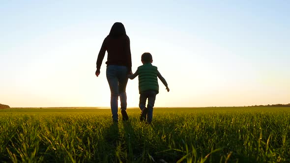 Happy Family. A Mother Runs, Holding Her Child's Hand, Across a Green Field at Sunset. Travel