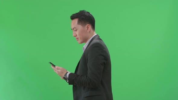 Side View Of Asian Business Man Use Mobile Phone While Walking On Green Screen Chroma Key