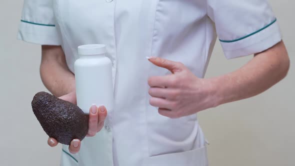 Nutritionist Doctor Holding Organic Avocado Fruit and Jar of Medicine or Vitamin or Omega 3 Capsules