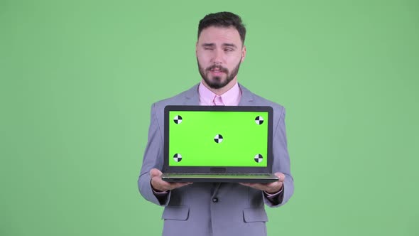 Happy Young Bearded Businessman Thinking While Showing Laptop