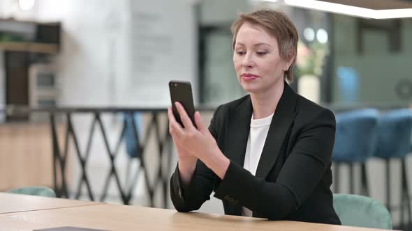Serious Old Businesswoman Using Smartphone in Office 