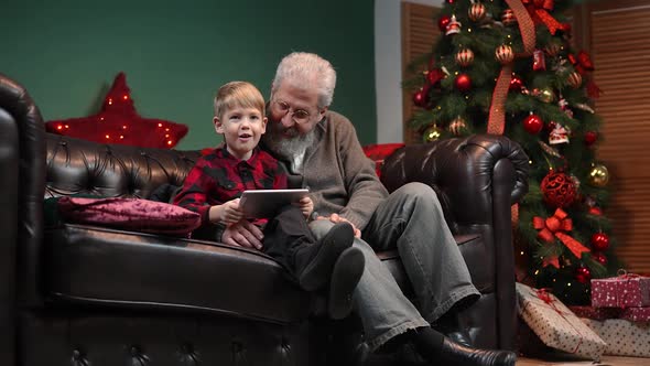 Elegant Old Man and Little Boy Talking on Video Communication on Tablet