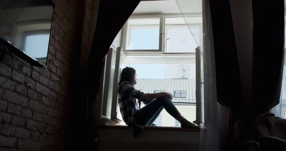 Young Woman Sitting on Window Sill and Enjoying Old Town View