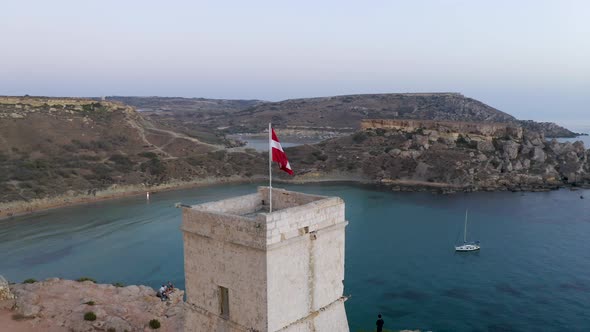 Flag of Maltese knights flying on a stone tower above a bay,aerial.