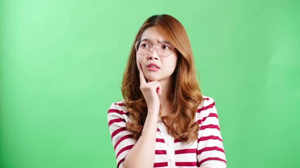 Young Asian woman with eyeglasses thinking, frowning and looking upwards, green screen background. T