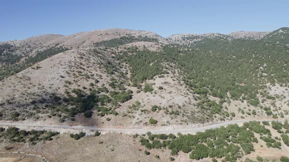 Aerial drone shot of the narrow curve road above rocky shore towards volcanic mountains.