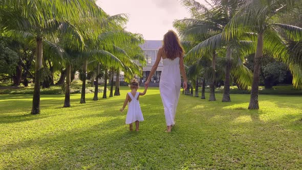 A Little Girl of Two Years Old in a White Dress Walks Her Mother Walk Hand in Hand Down a Park Trail