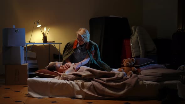 Wide Shot Girl Lying on Mattress in Basement in Bomb Shelter As Woman Stroking Hair of Child Calming