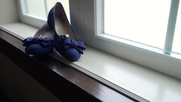 Bride wedding slippers and rings sitting on a large window sill with a left to right slider movement