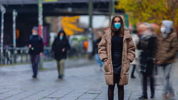 Time lapse of young woman wearing face mask and standing in city street, looking at camera alone