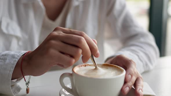 Hand Stirs Coffee Cappuccino With A Spoon Metal Spoon In A Cup Of Coffee Pushes The Foam And Whips